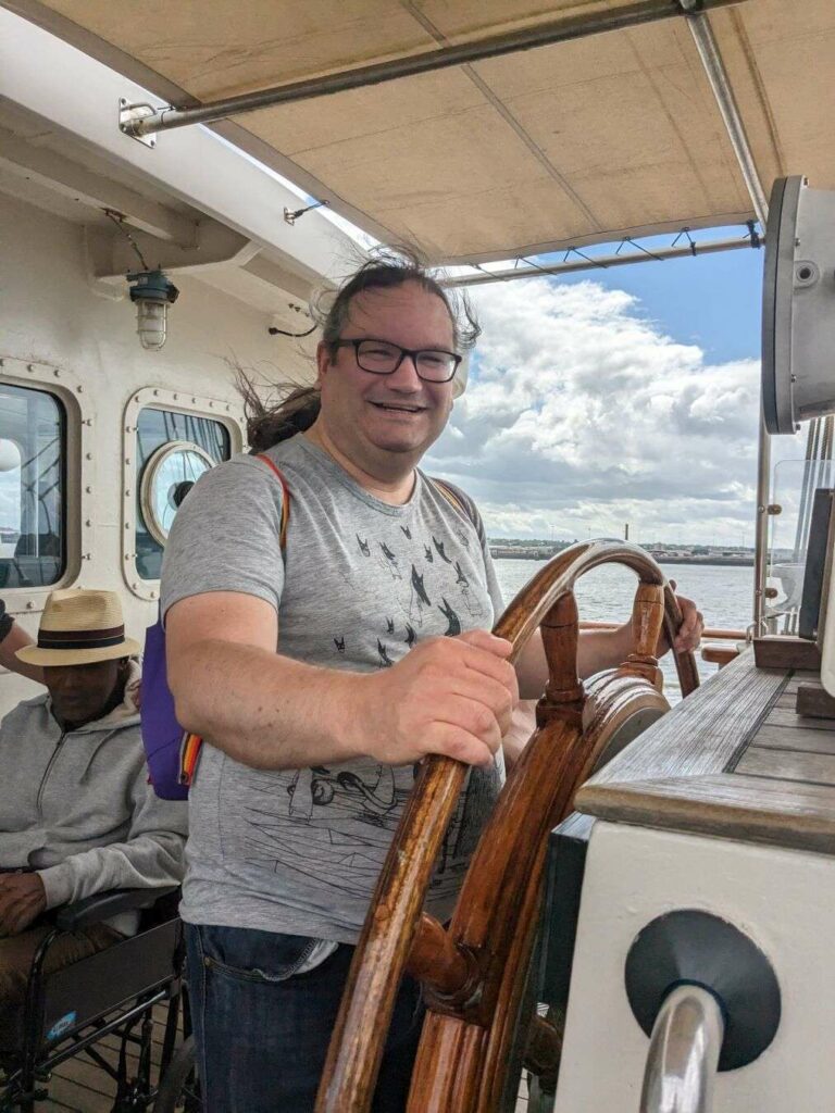 Me stood at the wheel of a ship wearing a grey t-shirt